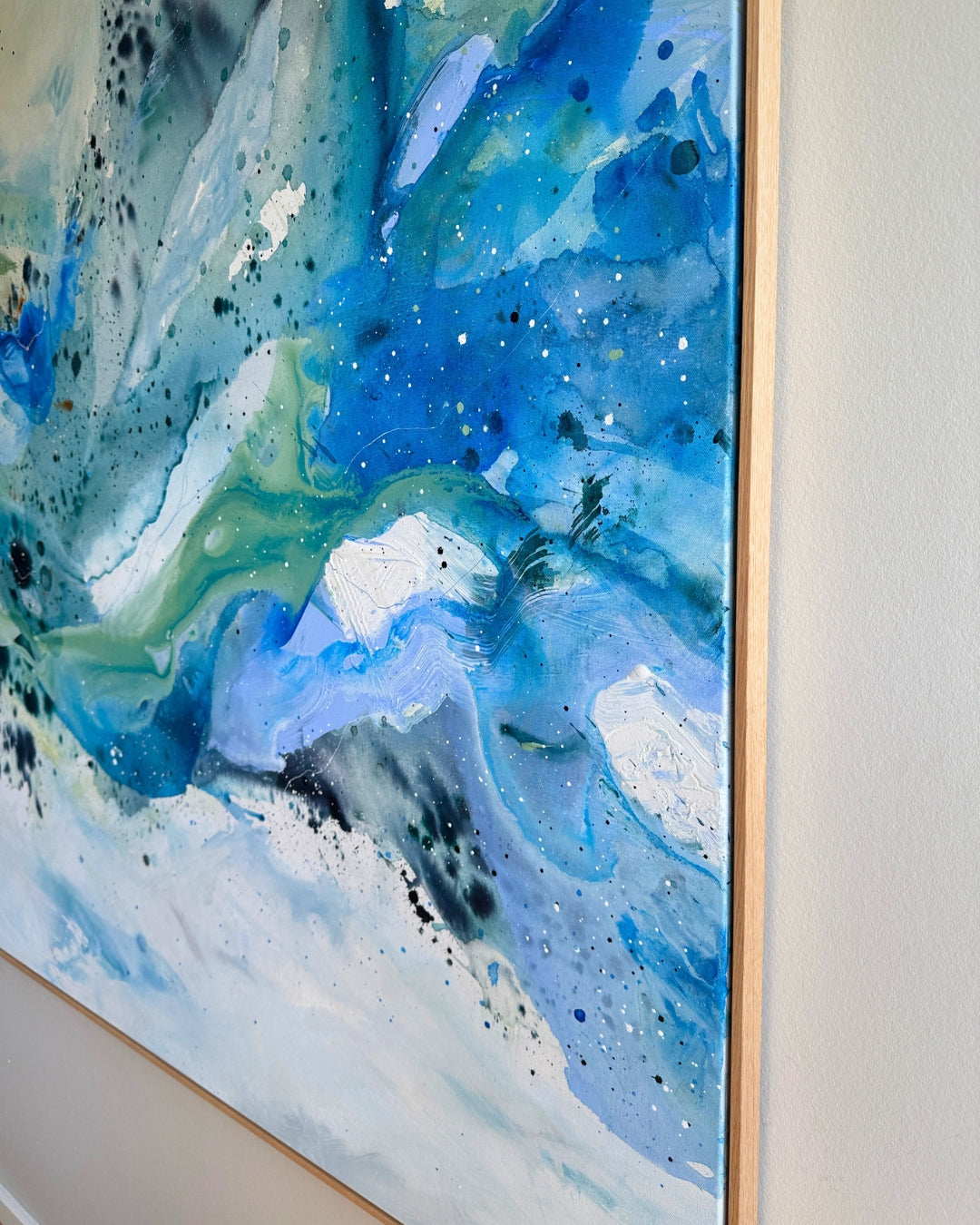 Close-up detail of original abstract canvas painting – fluid layers in cobalt blue, teal, sage green and white with fine paint splatter and glitter details, in natural oak float frame