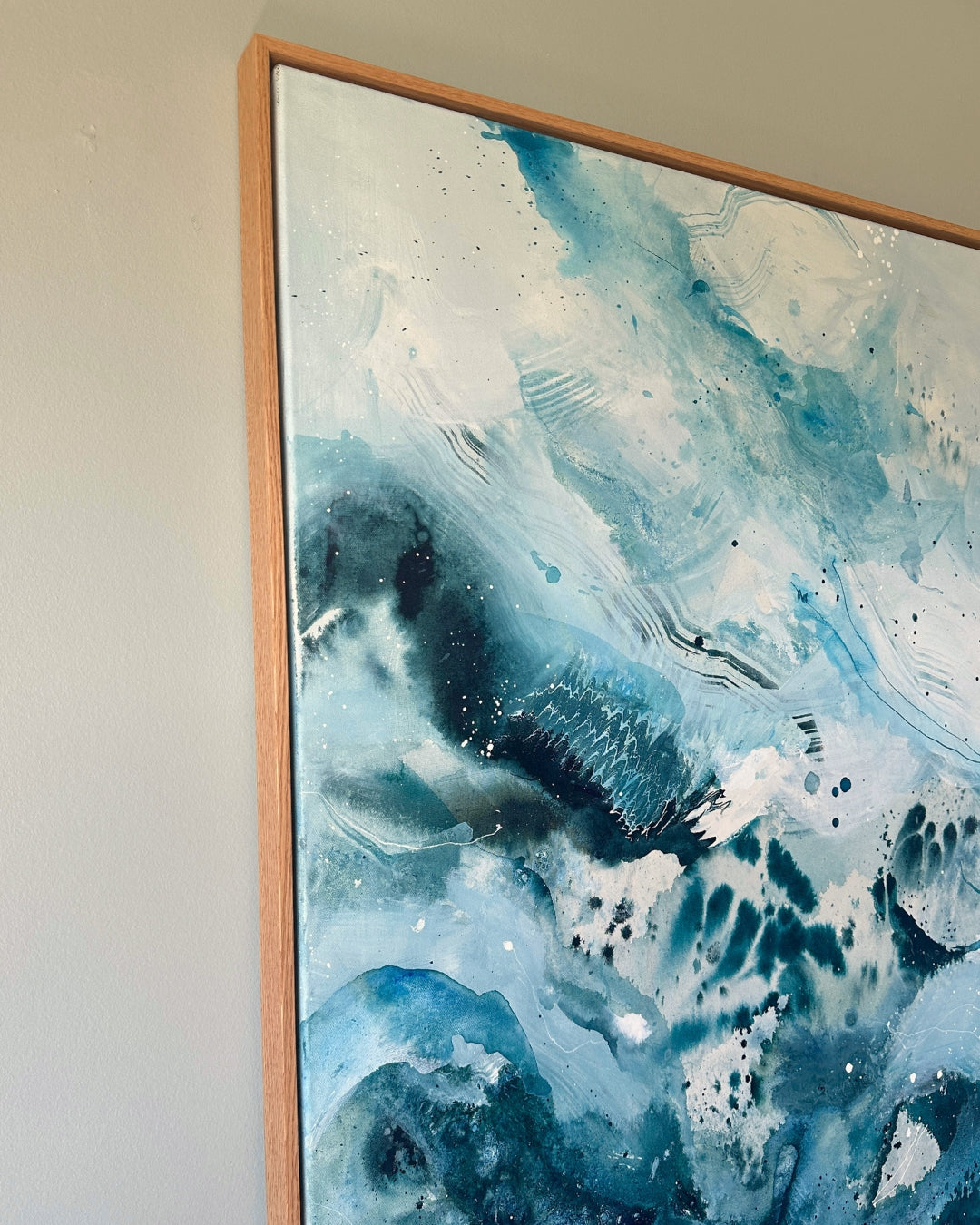 Corner detail of large original abstract canvas painting in natural oak float frame – expressive fluid layers in teal, cobalt blue and white with dynamic brushwork and fine line details