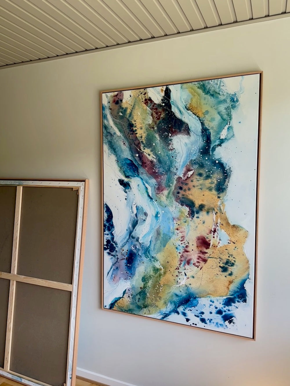 Abstract painting in warm gold and burgundy with cool teal and blue tones, 100x150 cm on canvas in oak frame – Soft #13 by Mette Lindberg, shown horizontally

