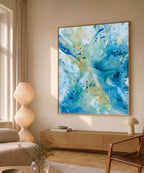 Original abstract canvas painting in soft blue, teal and warm gold tones, framed in natural oak. Shown in Nordic living room interior. One-of-a-kind artwork by Danish artist Mette Lindberg.