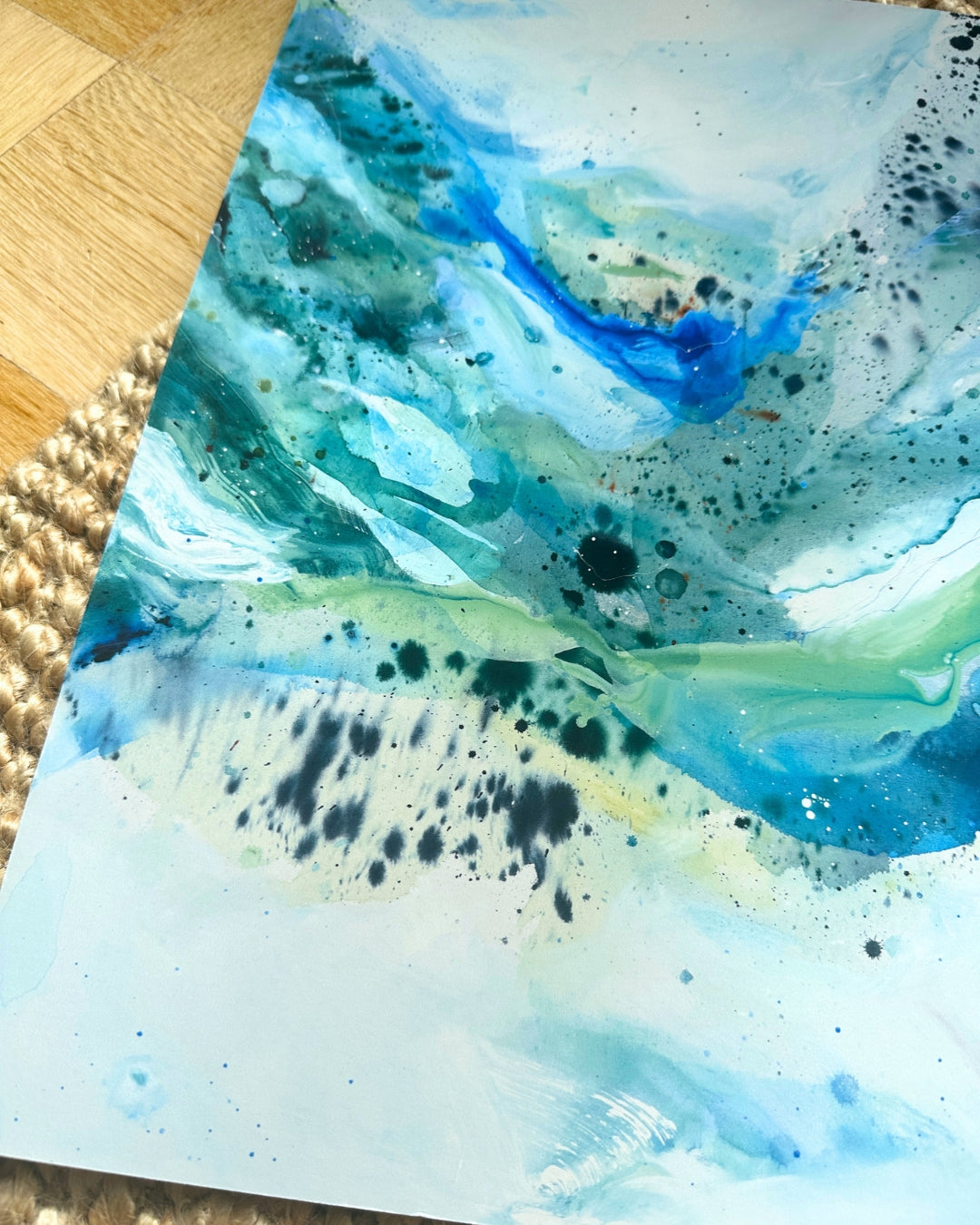 Close-up of abstract art print with flowing blue, teal and green paint, organic fluid shapes and black ink splatter