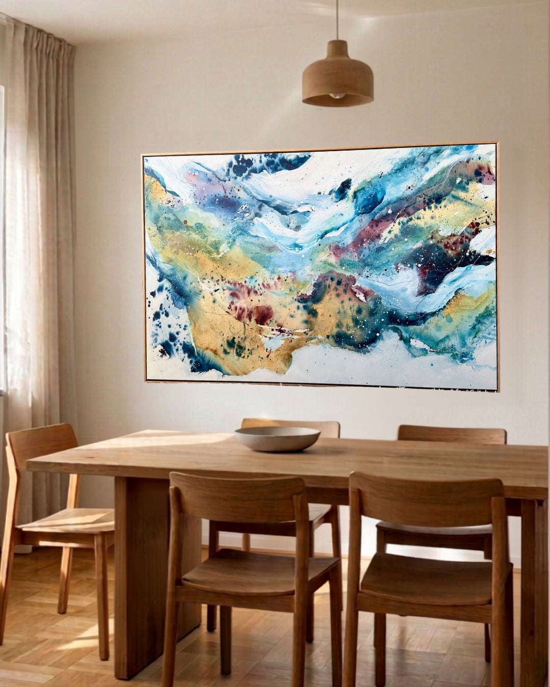Large abstract painting with flowing blue, teal, gold and burgundy tones with ink splashes, displayed in a natural wood frame above a Scandinavian dining table