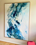 Large original abstract painting in vertical format hanging on white wall in Scandinavian room – expressive canvas artwork in teal, cobalt blue, navy and white with fluid dynamic brushwork, in natural oak float frame, with pink stool and parquet floor