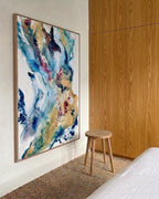 Large abstract painting in blue, gold and purple tones with oak frame, hung in a Nordic bedroom with oak wood panels and natural jute rug