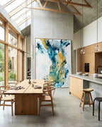 Monumental abstract painting on canvas in teal, blue and gold tones with oak frame, displayed in a contemporary open-plan dining room with floor-to-ceiling oak-framed windows, exposed timber roof trusses, concrete floors and Wishbone chairs