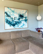 Large original abstract painting hanging above corner sofa on sage green wall – expressive canvas artwork in teal, deep blue and white with fluid brushwork and paint splatter, in natural oak float frame, shown in Scandinavian living room with pendant lamp and purple plant