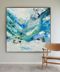large original abstract square canvas painting, 150x150 cm, in natural oak frame. Expressive fluid layers in teal, cobalt blue, sage green and white by Danish artist Mette Lindberg, shown in Scandinavian interior with oak chair.