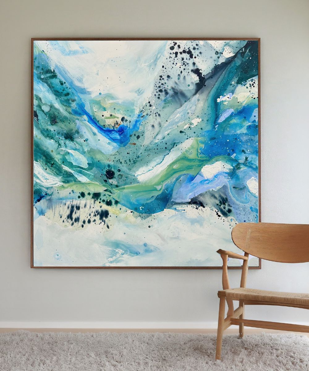 large original abstract square canvas painting, 150x150 cm, in natural oak frame. Expressive fluid layers in teal, cobalt blue, sage green and white by Danish artist Mette Lindberg, shown in Scandinavian interior with oak chair.