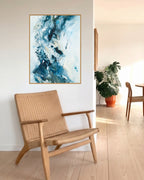 Abstract blue art print in oak frame above woven lounge chair by Mette Lindberg