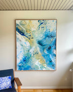 Large-scale abstract wall art on canvas, 100x150 cm, in natural oak frame – sweeping layers of teal, navy blue and golden yellow with expressive paint splatter by Danish artist Mette Lindberg, photographed in Nordic home setting