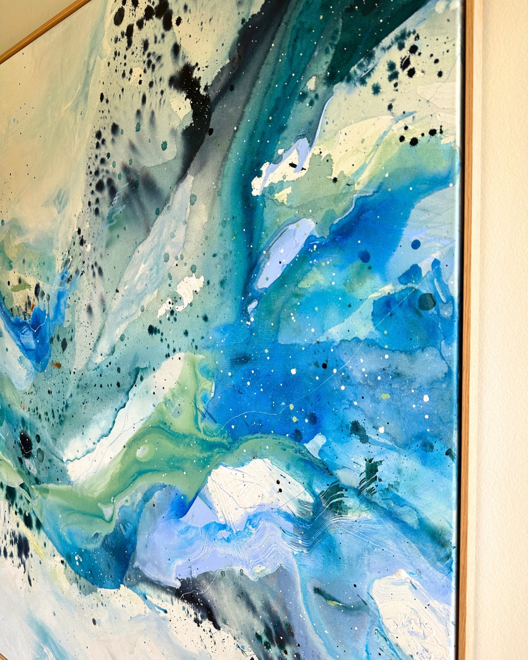 Corner detail of large original abstract canvas painting in natural oak float frame – expressive brushwork in teal, cobalt blue, sage green and white with black and white paint splatter and glitter details