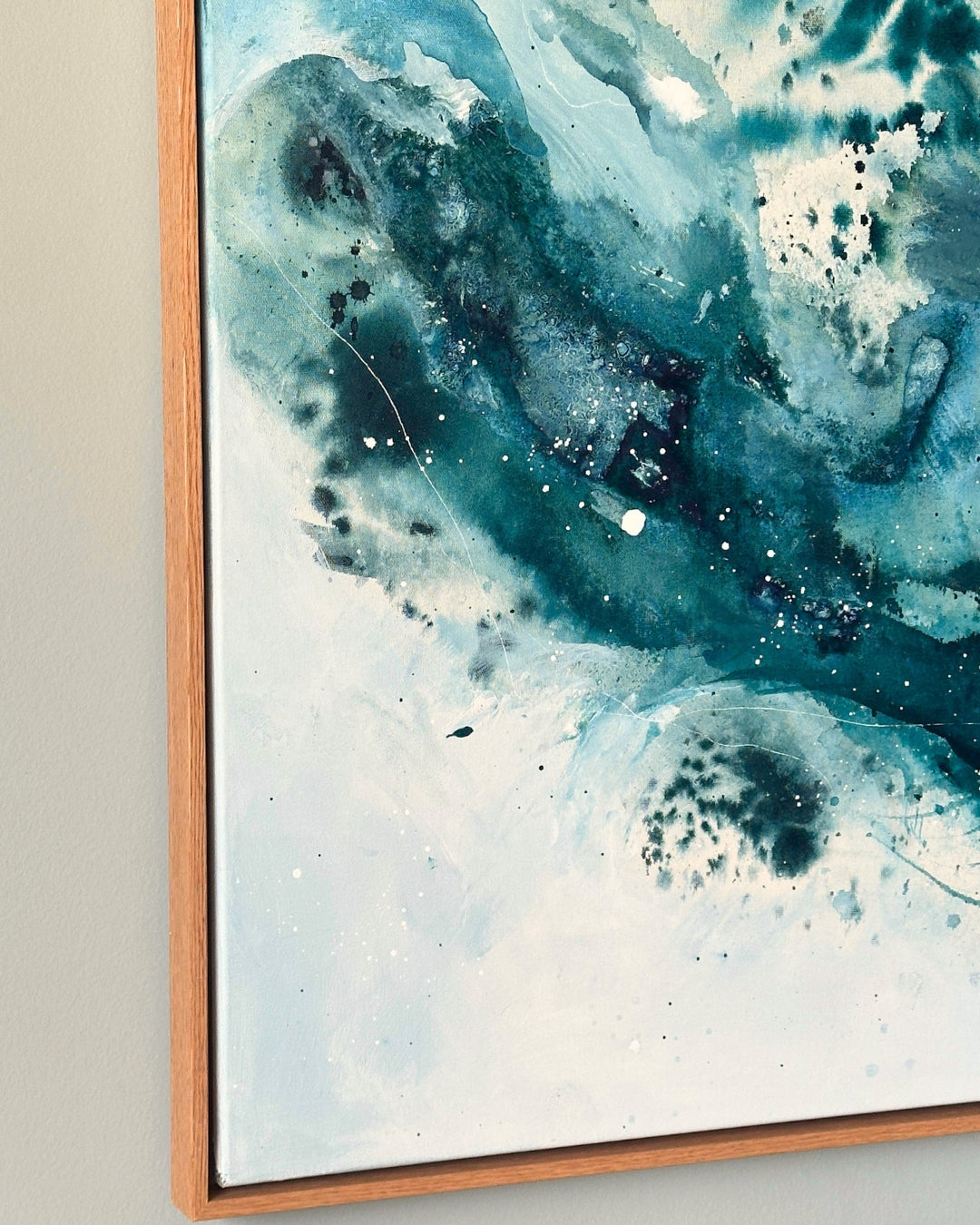 Corner detail of large original abstract canvas painting in natural oak float frame – expressive fluid layers in teal, cobalt blue and white with fine black and white paint splatter