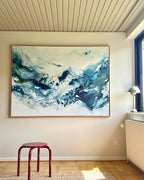 Large original abstract painting in horizontal format hanging on white wall in bright Scandinavian room – expressive canvas artwork in teal, cobalt blue and white with fluid brushwork, in natural oak float frame, with red stool, chrome floor lamp and parquet floor