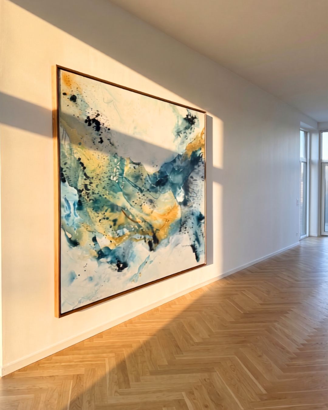 Large abstract painting on canvas in teal, blue and gold tones with oak frame, hung in a sunlit Nordic apartment with herringbone oak parquet floor and floor-to-ceiling windows