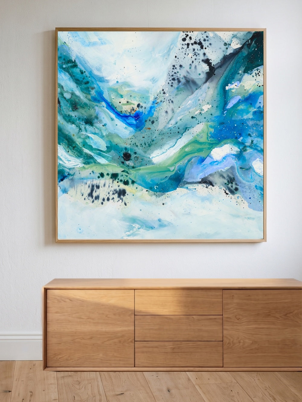 Large abstract art print place on a white wall above a cabinet in oak. The art print is in blue and green colours.