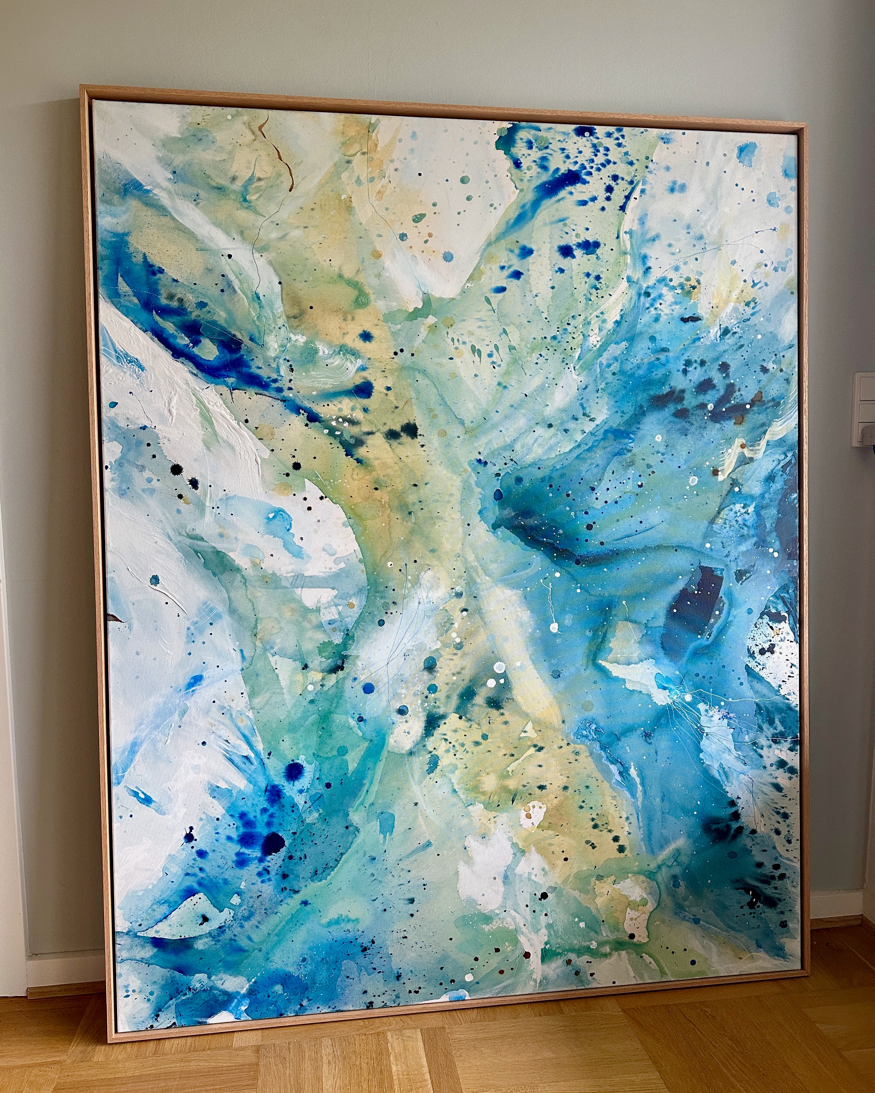 Large unique abstract wall art on canvas in oak frame. Vibrant splashes of teal, cobalt blue and golden tones by Danish fine artist Mette Lindberg. Original handmade painting, 100x150 cm.