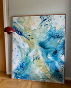 Original abstract canvas painting, 100x150 cm, in natural oak frame. Expressive fluid layers in bright teal, sky blue, white and warm gold by Danish artist Mette Lindberg, shown in Nordic home setting.