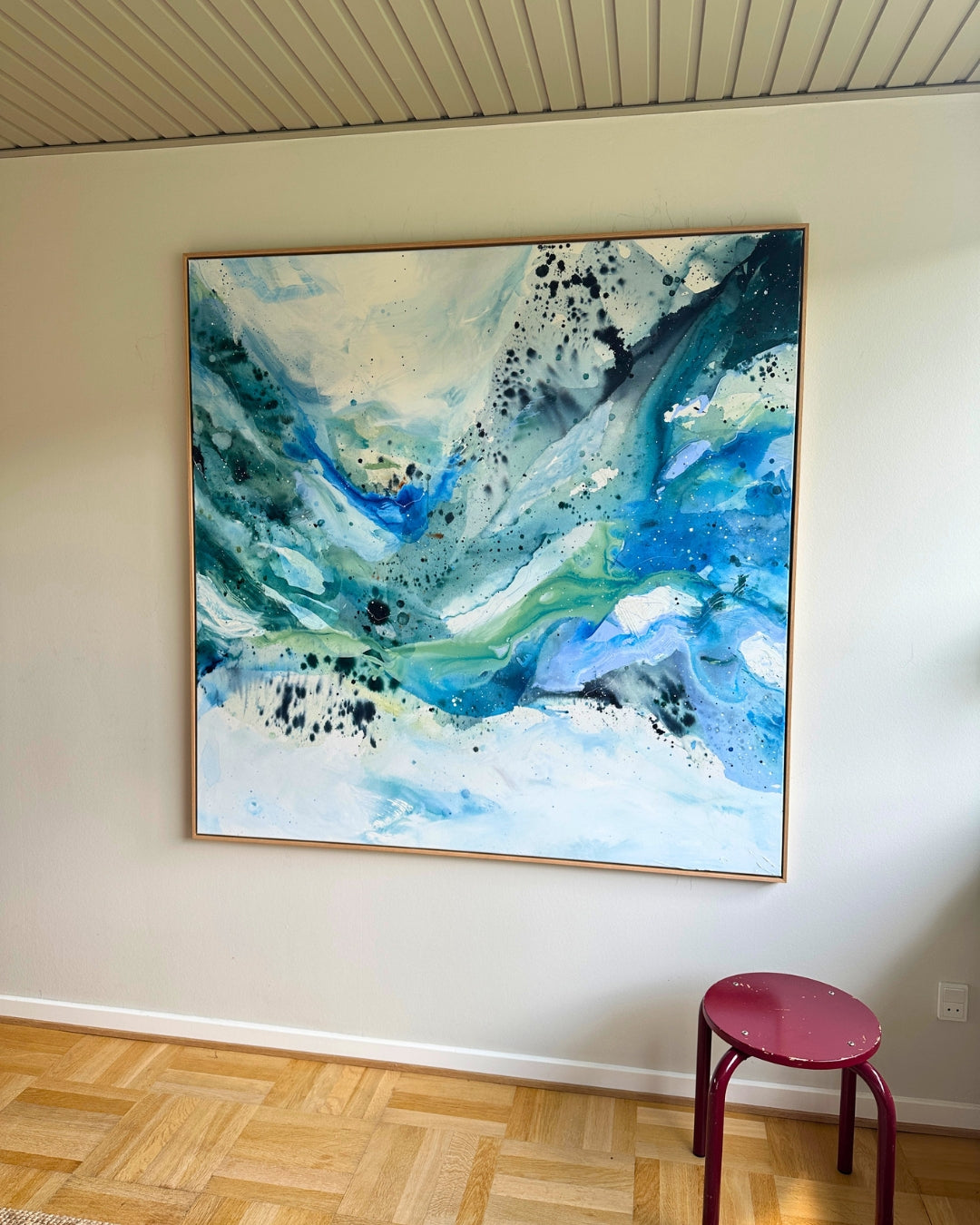 Original abstract painting on canvas in flowing teal, sky blue and white tones, in natural oak float frame – expressive brushwork and ink splatter, displayed in bright Scandinavian interior with parquet floor