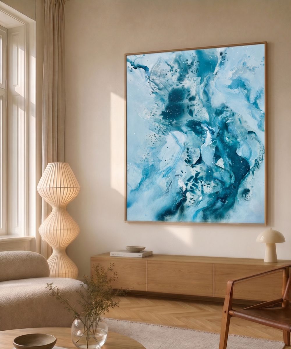 Original abstract canvas painting in soft blue, teal and warm gold tones, framed in natural oak. Shown in Nordic living room interior. One-of-a-kind artwork by Danish artist Mette Lindberg