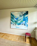 Modern original abstract canvas artwork in deep teal, blue and green tones, in natural oak float frame – dynamic paint splatter and fluid layers, photographed in Nordic room with wooden parquet floor